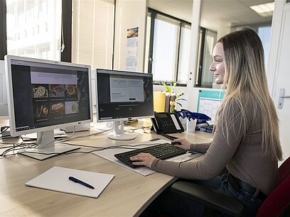 Eine junge Frau erstellt am Computer eine Website mit Produkten.
